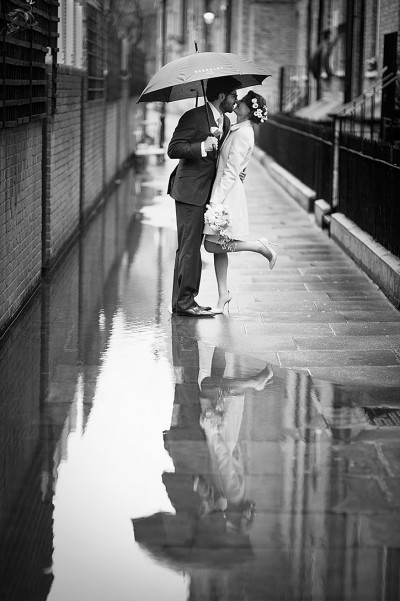 Couple reflected in a puddle as they kiss under an umbrella in the rain.
