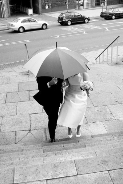 Bride and her father huddle under an umbrella as they approach the church.