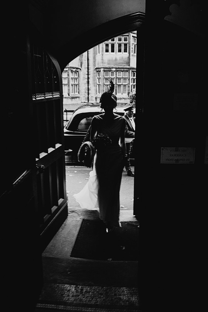 Bride makes a perfect silhouette as she enters the chapel wearing a designer hat.