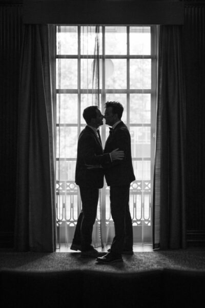 two grooms silhouetted as they kiss in front of the window in the Westminster room at Marylebone Town Hall