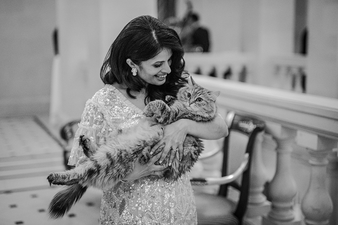 lilibet-lanesbourough-cat-wedding - Wedding photographer London Woman in a sequined wedding dress gently cradles a fluffy cat, smiling in an elegant indoor setting.