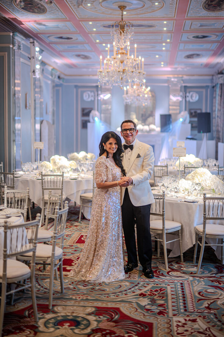 wedding-photography-lanesbourough-hyde-park - Wedding photographer London Couple in formalwear posing arm in arm in a luxurious ballroom with chandeliers and white floral centerpieces.